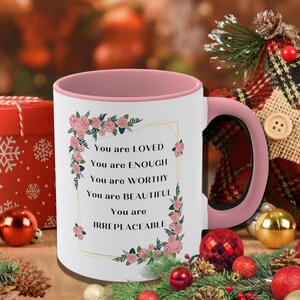 May include: A pink and white ceramic mug with a black handle. The mug has a floral design and the text "You are LOVED, You are ENOUGH, You are WORTHY, You are BEAUTIFUL, You are IRREPLACEABLE".