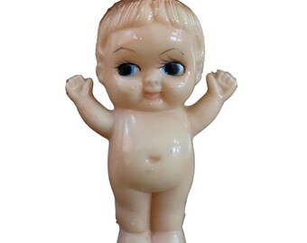 May include: A vintage, nude-colored baby doll with blue eyes and a smiling expression. The doll has its arms raised and short, light-colored hair. The doll is standing upright.