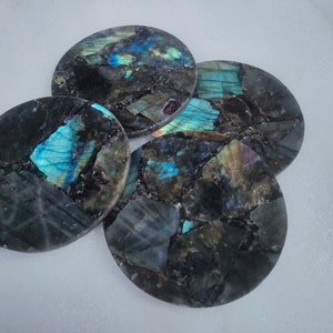 May include: Four round coasters made of labradorite stone. The coasters have a dark gray background with iridescent blue, green, and gold flecks.