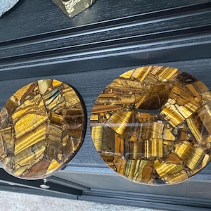 May include: Two round coasters made of tiger's eye stone. The coasters are a mosaic of gold, brown, and black tiger's eye pieces.