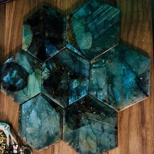 May include: A cluster of six hexagonal tiles made of labradorite stone, featuring a polished surface with deep teal, blue, and dark green iridescent flashes. The tiles are arranged in a honeycomb pattern, showcasing natural mineral inclusions and veins.