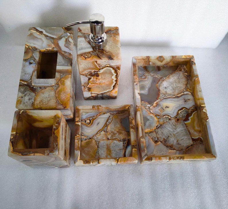 Op de afbeelding: Een vijfdelige badkamerset gemaakt van agaat. De set bestaat uit een zeepdispenser, een tandenborstelhouder, een tissueboxhouder en twee dienbladen. Agaat is een natuurlijk materiaal met verschillende kleuren en patronen.