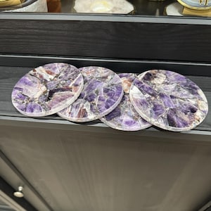 May include: Four amethyst coasters featuring a purple and white swirl pattern. The coasters are crafted from natural stone and are ideal for safeguarding your furniture from scratches and spills.