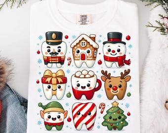 May include: White t-shirt featuring a colorful graphic of cartoon teeth dressed as Christmas characters, including a nutcracker, gingerbread house, snowman, gift, mug of cocoa, reindeer, elf, candy cane, and Christmas tree. The shirt has the "Comfort Colors" brand tag.