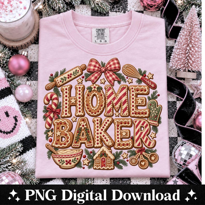 May include: A light pink short-sleeve t-shirt featuring a graphic of gingerbread-style letters spelling HOME BAKER. The design includes a rolling pin, whisk, candy cane, mixing bowl, and gingerbread house, all accented with red and white patterns.