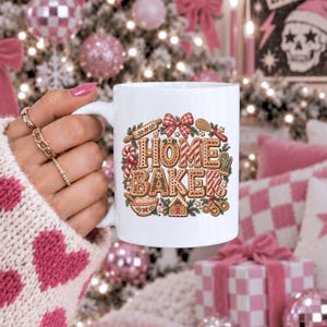 May include: A white ceramic mug featuring a colorful graphic of gingerbread-style letters spelling HOME BAKER, surrounded by illustrations of a rolling pin, whisk, candy cane, mixing bowl, measuring spoons, and a small gingerbread house.