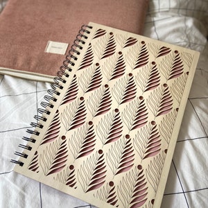 May include: A wooden spiral bound notebook with a pink and white leaf pattern. The leaves are cut out of the wood, revealing the pink background.