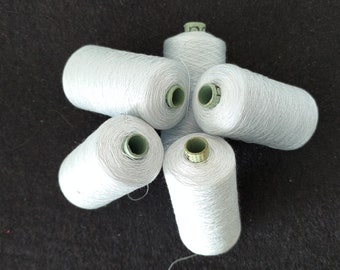 Könnte beinhalten: Fünf Spulen mit hellblauem Garn, die auf einer schwarzen Oberfläche in Sternform angeordnet sind.