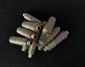 Könnte beinhalten: Ein Stapel bunter Garnrollen, jede mit einem anderen Muster aus Regenbogenfarben. Die Rollen sind in einem zufälligen Muster angeordnet, wobei sich einige Rollen überlappen.