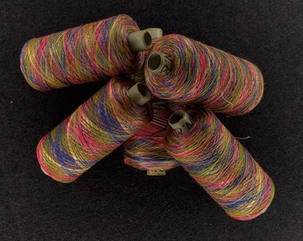 Könnte beinhalten: Fünf Spulen mit buntem Garn, jede mit einem anderen Muster aus rosa, blau, grün und goldenem Garn. Die Spulen sind in einem Kreis auf einem schwarzen Hintergrund angeordnet.