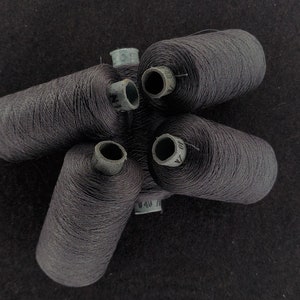 Puede incluir: Cinco carretes de hilo gris oscuro, cada uno con una etiqueta blanca y texto negro.