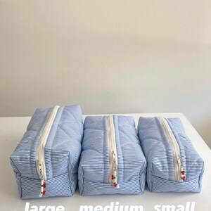 May include: Three quilted striped zippered pouches in blue and white with red accents. The pouches are labeled "large", "medium", and "small" from left to right.