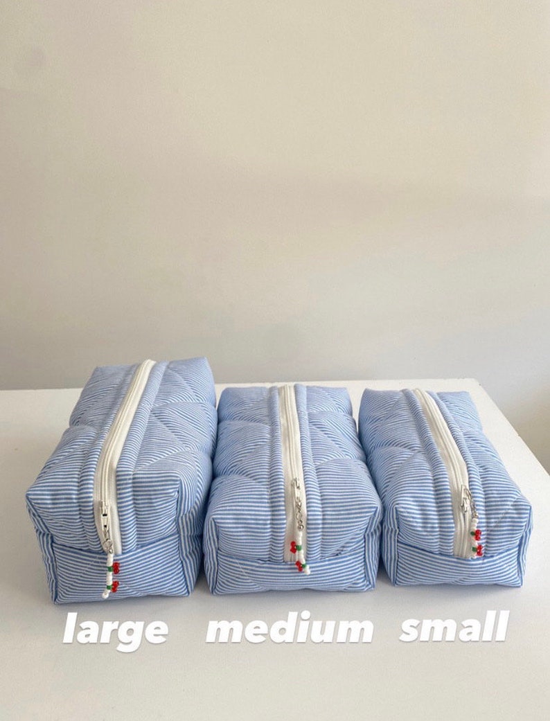May include: Three quilted striped zippered pouches in blue and white with red accents. The pouches are labeled "large", "medium", and "small" from left to right.