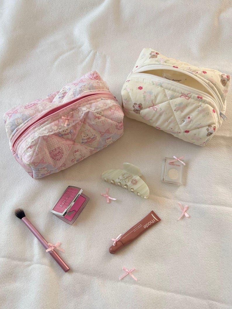 May include: Two quilted cosmetic bags, one pink and one cream, with matching makeup accessories. The pink bag features a pattern with characters and lace trim. Accessories include a blush compact, lip gloss, a makeup brush, and a hair clip, all adorned with pink bows.