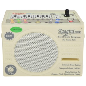 Puede incluir: Tanpura electrónica Raagini Digital de color crema con altavoz, botones de control y el texto "Raagini DIGITAL Electronic Tanpura By, Sound Labs". Cuenta con una pegatina "NEW" y un sello "INSPECTED". Incluye ajustes digitales para volumen, tono, tono fino y tempo.
