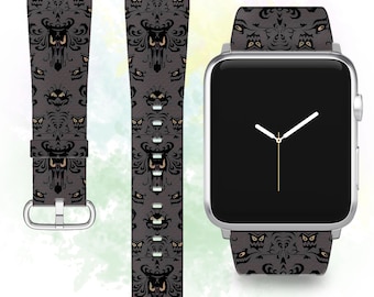 May include: A black and gray patterned Apple Watch band with a repeating design of a haunted mansion. The band is shown on a silver Apple Watch.