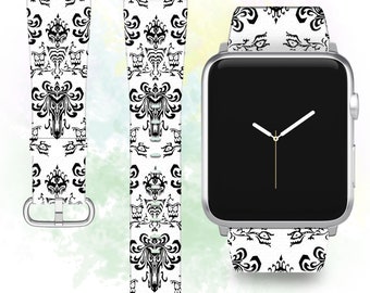 May include: A silver Apple Watch with a white and black patterned band. The band features a repeating pattern of a ghostly figure and a haunted house.