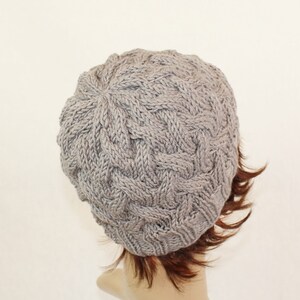 May include: A gray knitted beanie with a cable knit pattern. The beanie is shown from the back.