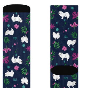 May include: A pair of navy blue socks with a repeating pattern of white dogs, pink flowers, and green leaves. The socks have black cuffs and toes. The design is a whimsical and colorful addition to any wardrobe.