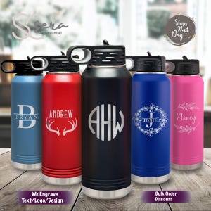 May include: Five stainless steel water bottles with different colored exteriors and personalized engravings. The bottles have a black lid with a carrying handle. The engravings include names, initials, and designs.