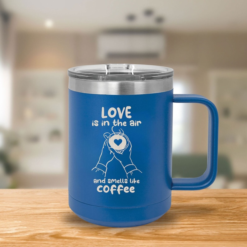 May include: Blue stainless steel travel mug with a white design that says "Love is in the air and smells like coffee". The mug has a handle and a lid.
