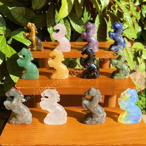 以下が含まれることがあります： 緑、黄色、黒、青など、さまざまな色の小さな彫刻されたクリスタル馬の置物のコレクション。 馬は、緑の葉の背景に対して、木製の棚に展示されています。