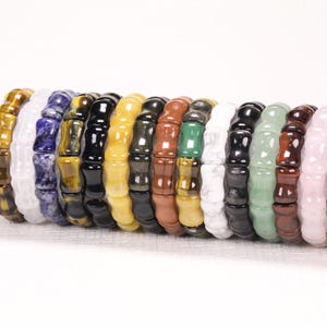 May include: A collection of fifteen stretch bracelets made from various polished gemstones, including tiger's eye, sodalite, white quartz, black obsidian, yellow jade, green aventurine, red jasper, and rose quartz, featuring a distinct bamboo-like shape.