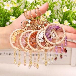 May include: A collection of five circular keychains featuring a wire-wrapped tree design with gemstone chips in yellow, pink, orange, white, and purple. Each keychain has a gold-tone metal clasp and dangling beaded strands with crystal accents.