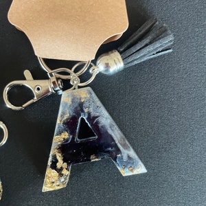 May include: A black and gold resin letter A keychain with a black tassel and silver key ring.
