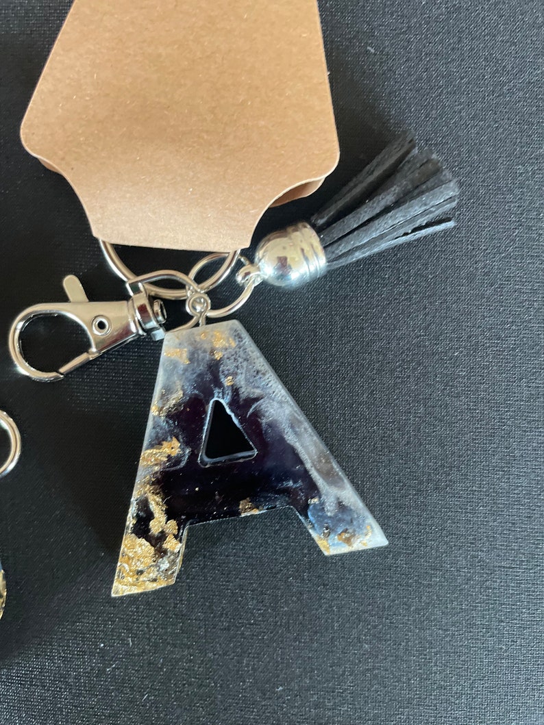 May include: A black and gold resin letter A keychain with a black tassel and silver key ring.