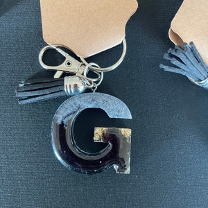 May include: Black and gold resin letter G keychain with a black tassel.
