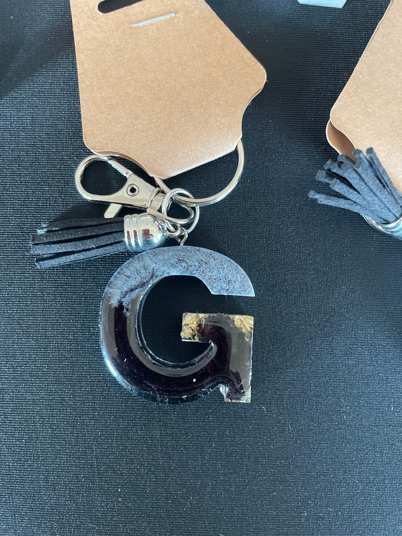 May include: Black and gold resin letter G keychain with a black tassel.