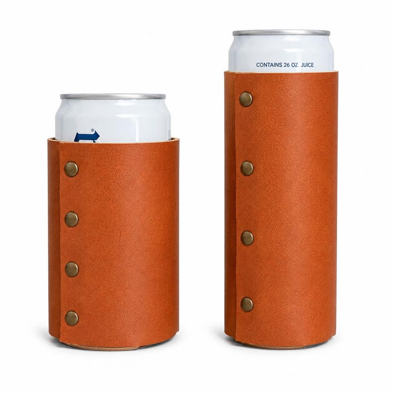 May include: Two brown leather can coolers with brass-colored rivets. One cooler is shorter, and the other is taller. The cans inside are white with blue graphics and text that reads "CONTAINS 26 OZ. JUICE."