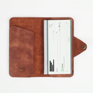Könnte beinhalten: Ein braunes Leder-Scheckbuch-Etui mit einer Klappe und einem Druckknopfverschluss. Das Etui hat ein Fach auf der linken Seite und einen Scheckbuchhalter auf der rechten Seite. Der Scheckbuchhalter enthält einen Scheck der TD Bank mit der Nummer 1791.