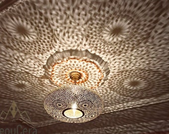 May include: A round, gold-colored Moroccan pendant light fixture with intricate cut-out designs. The light casts a patterned shadow on the ceiling.