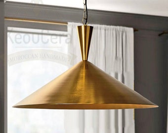 Op de afbeelding: Een gouden hanglamp met een brede, conische kap hangt aan een ketting boven een eettafel. De lamp hangt boven een tafel met een kom met vetplanten.