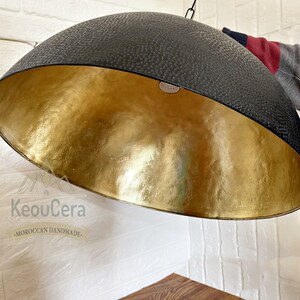 May include: A black and gold dome-shaped pendant light fixture with a textured black exterior and a gold interior. The light fixture is hanging from a white ceiling.