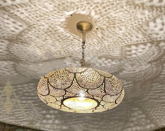 May include: A gold Moroccan pendant light with a round, intricate, and patterned design. The light casts a beautiful shadow pattern on the ceiling.
