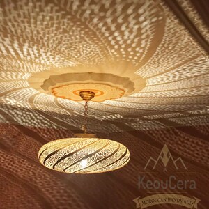 May include: A gold-colored, round, Moroccan pendant light fixture with a decorative, intricate, cut-out design. The light fixture is hanging from a chain and casts a geometric pattern on the ceiling.