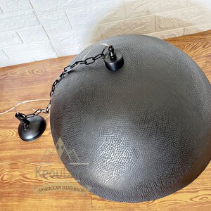 May include: Black metal pendant light with a hammered finish and a chain hanging from the ceiling. The light is round and has a textured surface.