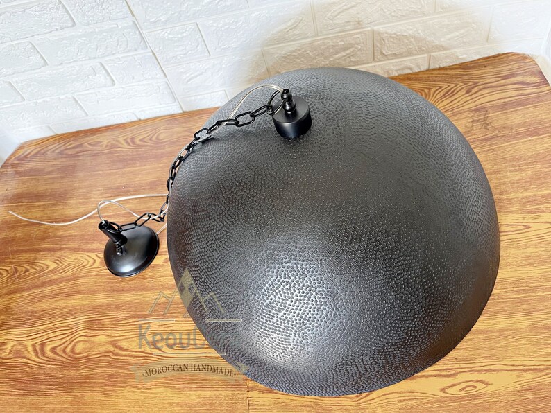 May include: Black metal pendant light with a hammered finish and a chain hanging from the ceiling. The light is round and has a textured surface.