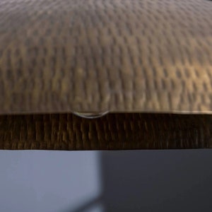 May include: A close-up of a hammered brass tray with a textured surface.