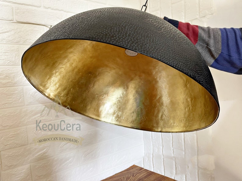 May include: A black and gold dome-shaped pendant light fixture with a textured black exterior and a gold interior. The light fixture is hanging from a white ceiling.
