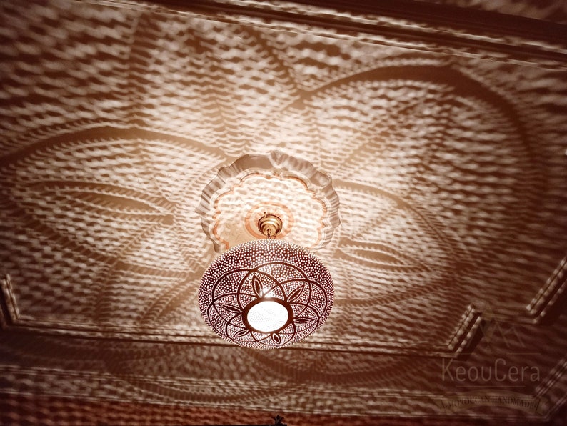 May include: A round, gold-colored metal ceiling light fixture with a geometric pattern. The light casts a patterned shadow on the ceiling.