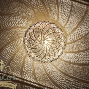 May include: A gold-toned Moroccan pendant light fixture with a circular, geometric design. The light fixture casts intricate shadows on the ceiling.