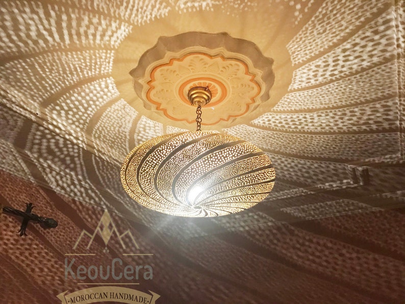 May include: A gold-toned metal ceiling light fixture with a circular, patterned shade. The light casts a geometric pattern on the ceiling.