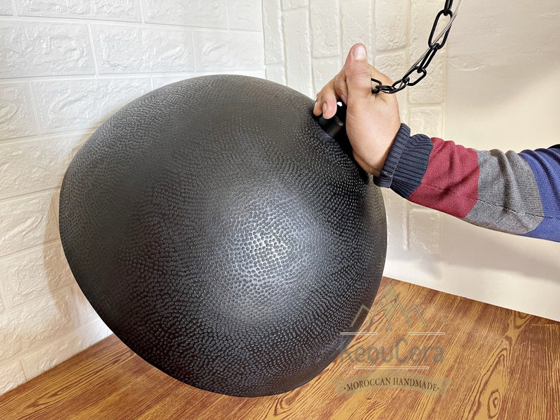 May include: Black metal pendant light fitting with a hammered texture. The light fitting is hanging from a chain.