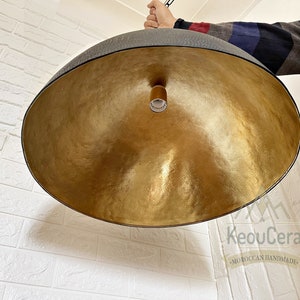 May include: A large, round, gold-coloured pendant light fitting with a black metal frame. The light fitting is hanging from a ceiling and has a simple, modern design.
