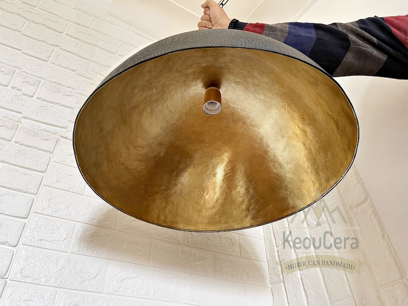 May include: A large, round, gold-coloured pendant light fitting with a black metal frame. The light fitting is hanging from a ceiling and has a simple, modern design.