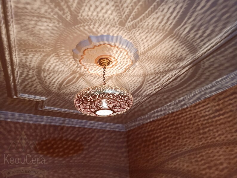 May include: A round, brass pendant light with a geometric pattern hangs from a chain. The light casts intricate shadows on the ceiling.